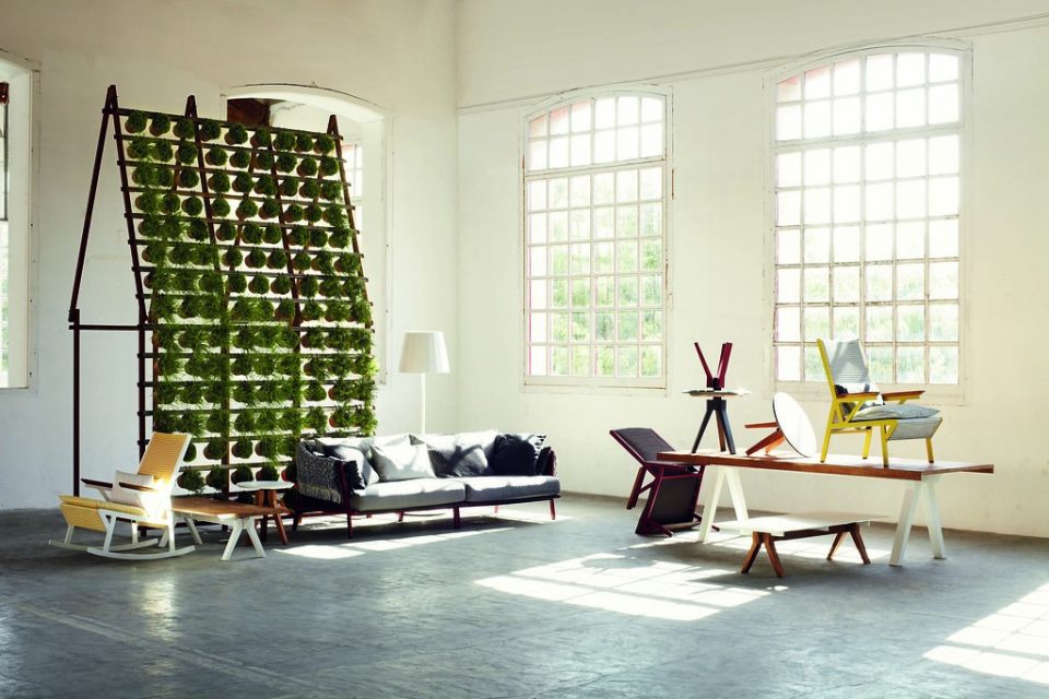 Hanging plant wall with a grey couch, yellow chairs, picnic tables, and big windows