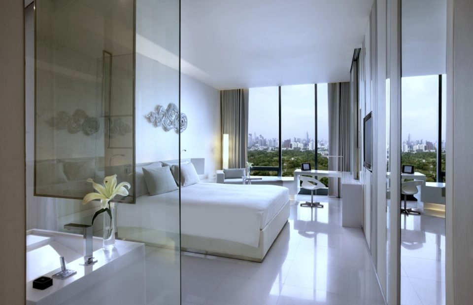 White hotel room over looking a city with big glass windows and glass bathroom cover 