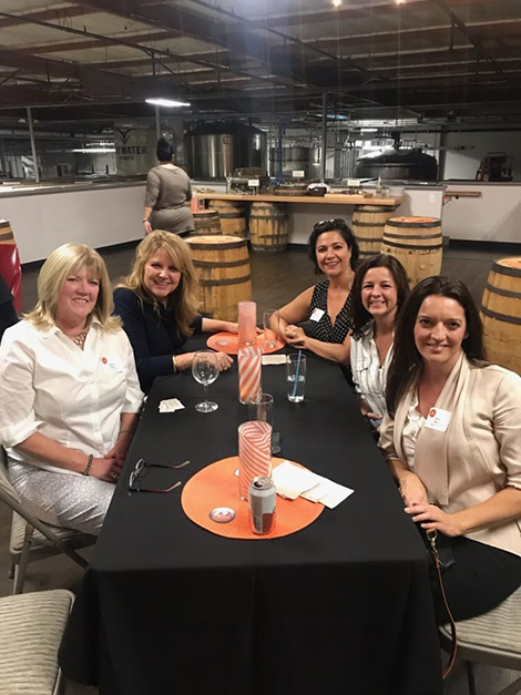 Five women including 4 alumna and the school's financial aid director, pose for a photo at their table