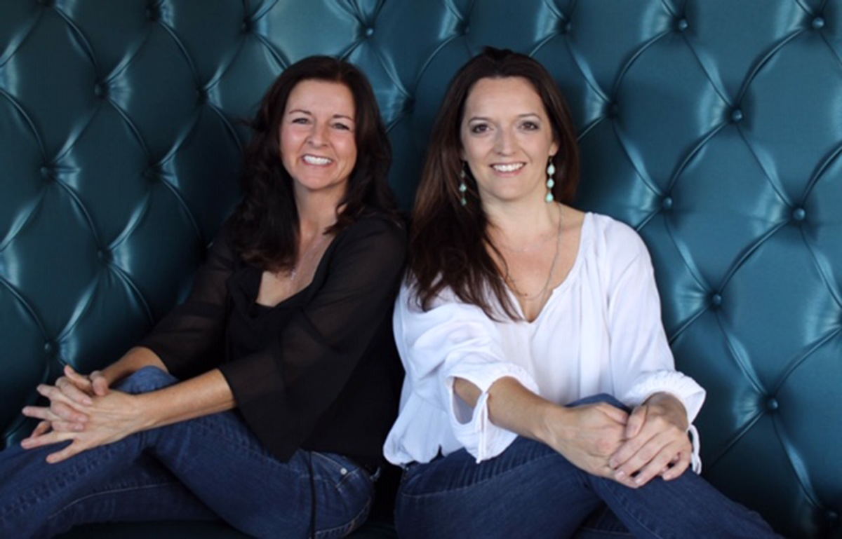 Two smiling interior designers posing side-to-side on a blue booth located inside restaurant Public House 131. Gina Florentino (left) and Alynn Etzler (right)
