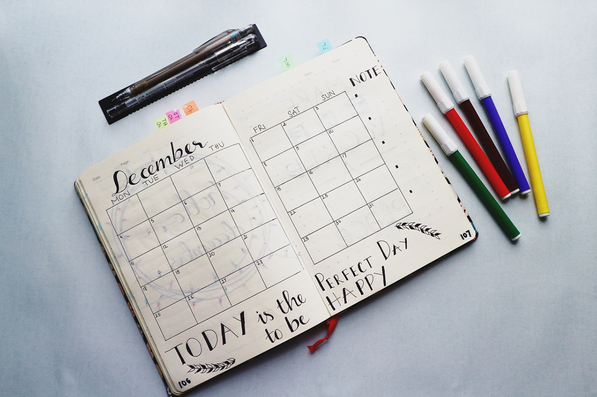 A day planner on a table, opened to the month of December, with a few markers laying around it