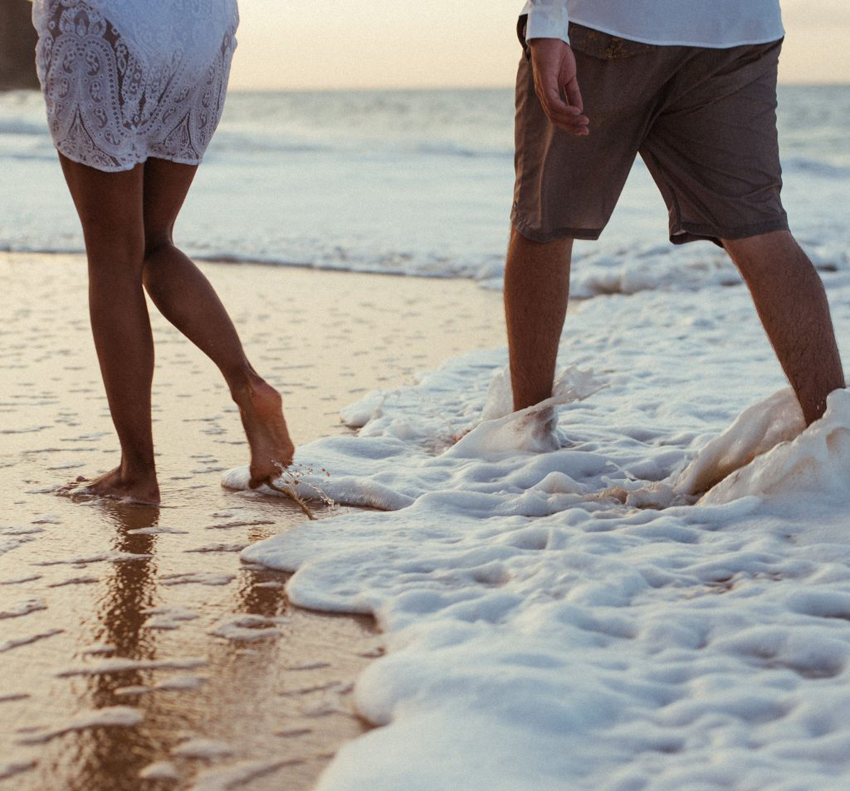 Two people are walking along the shore, water coming in 