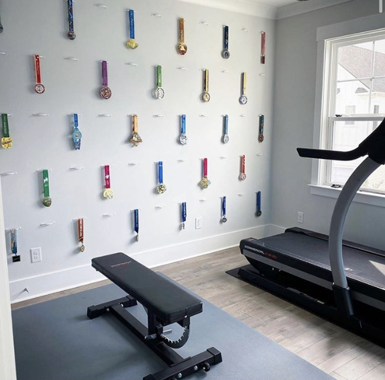 An in-home gym with a flat bench and a treadmill. On the wall behind the equipment, awards and medals hand on hooks.